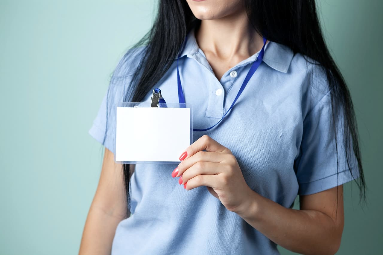 A hand holding up a blank white ID badge on a lanyard