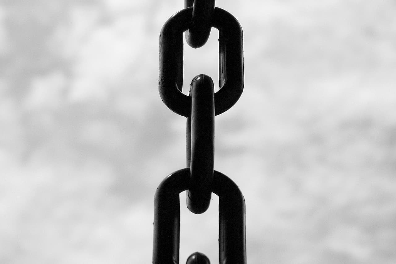 Black and white close-up of a hanging metal chain against a cloudy sky