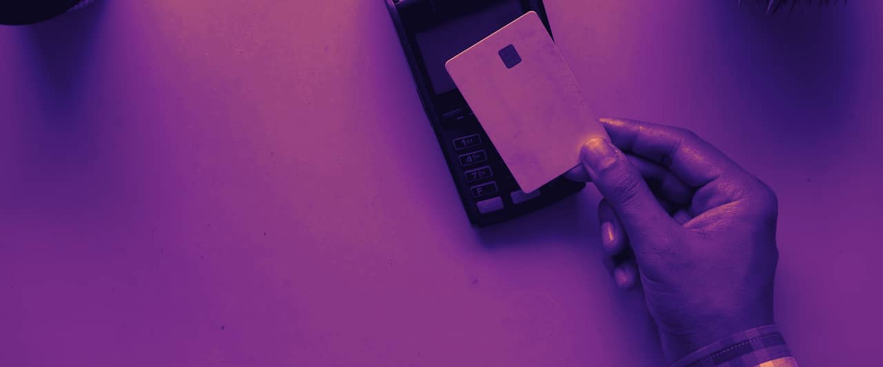 A hand holding a blank card next to a payment terminal on an orange table
