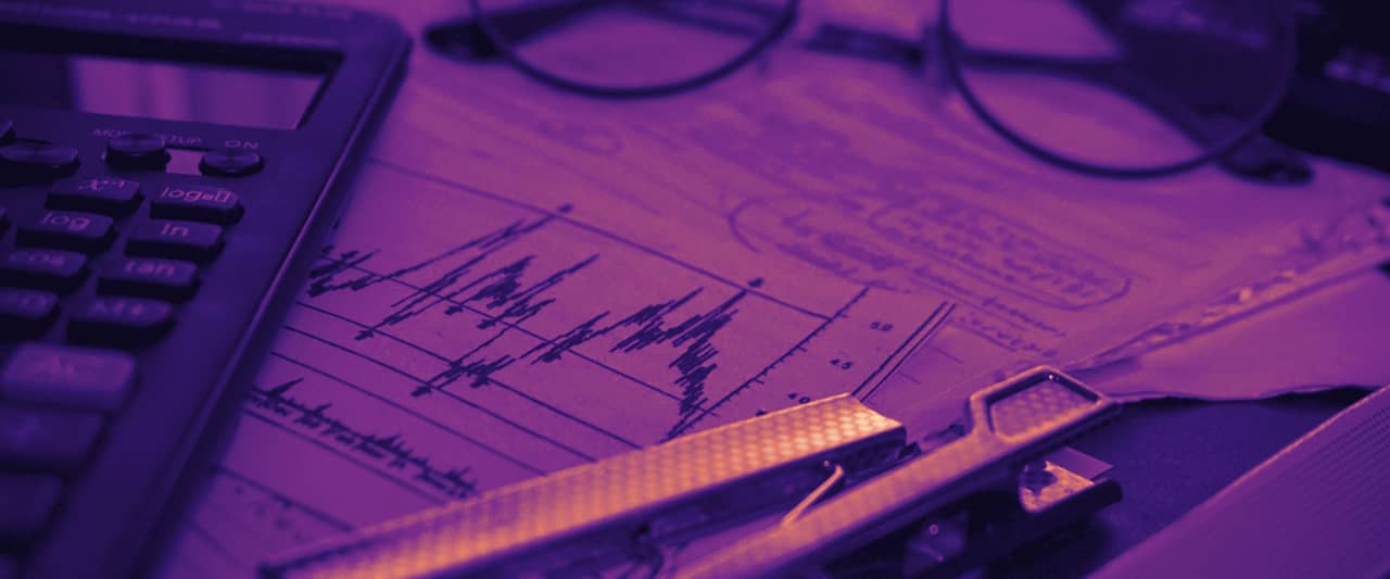 A desk with a calculator, printed charts, eyeglasses and office supplies