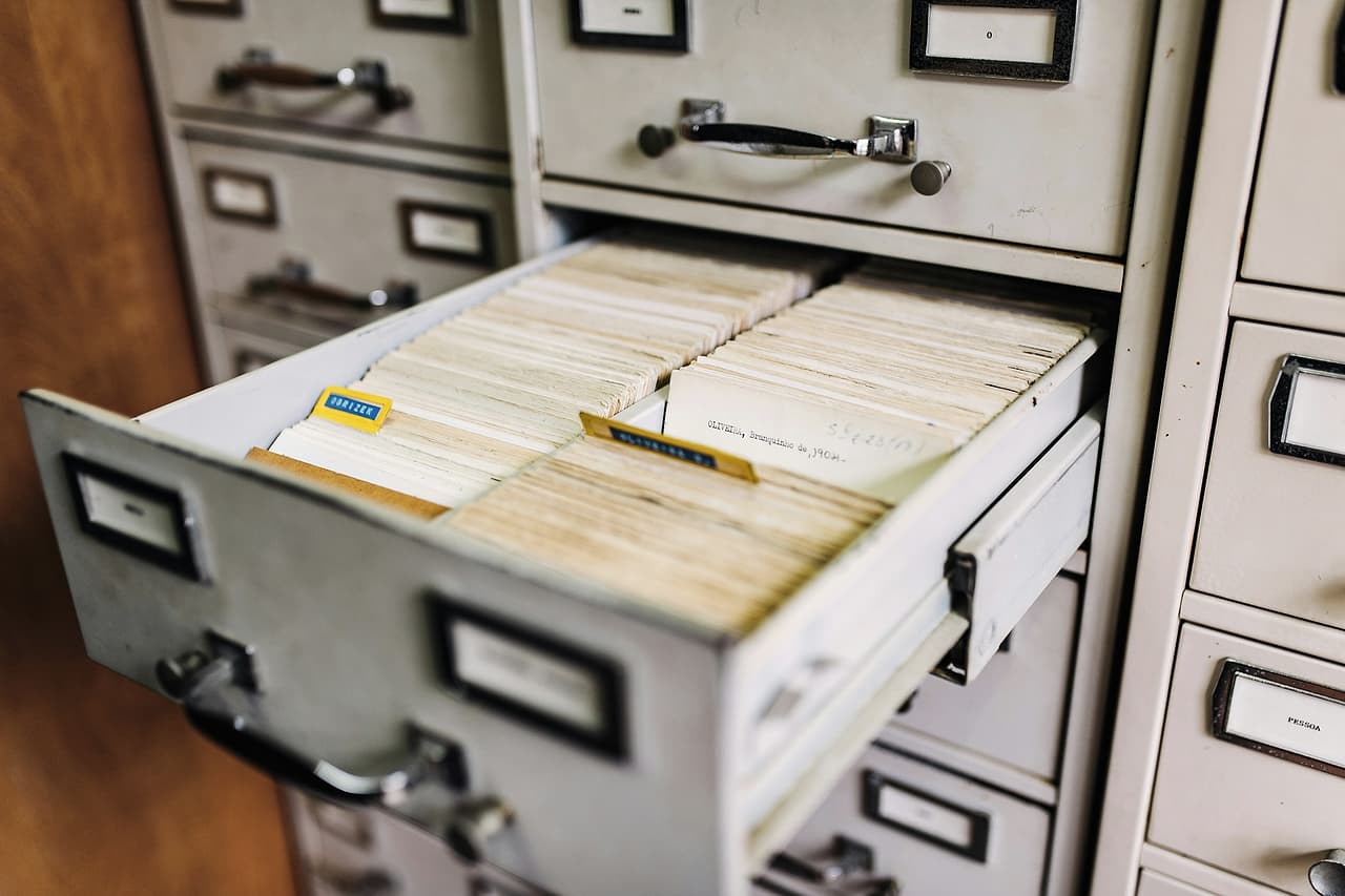 An open drawer of a grey filing cabinet packed with index cards