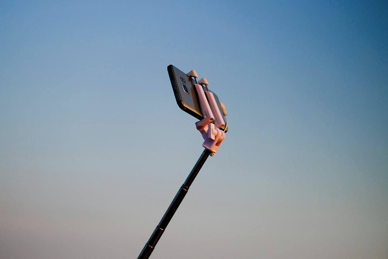 A smartphone held up on a selfie stick against an evening sky