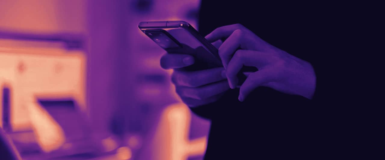 A hand holding a smartphone, the screen turned away from the camera