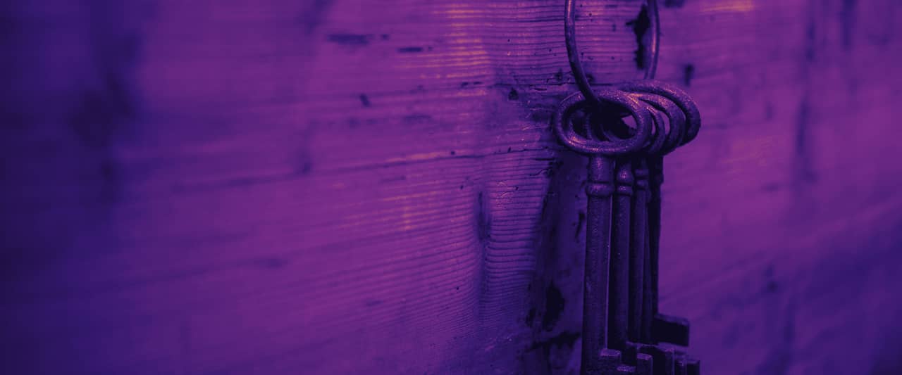 A bunch of old iron keys hanging from a nail on a wooden wall