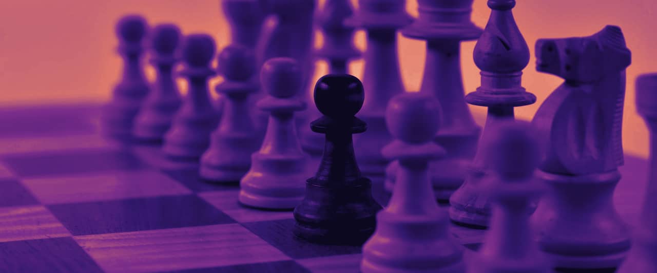 Wooden chess pieces lined up on a board, one dark pawn among light pieces