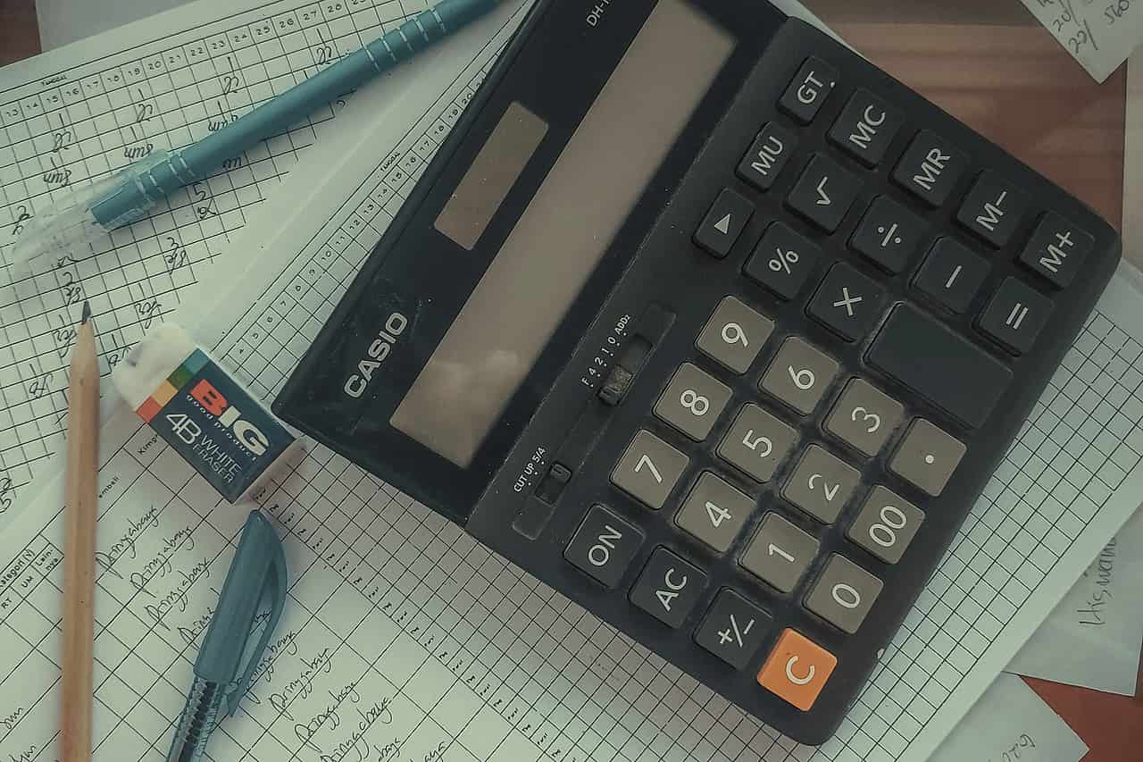 A calculator lying on a pile of papers with pencils beside it