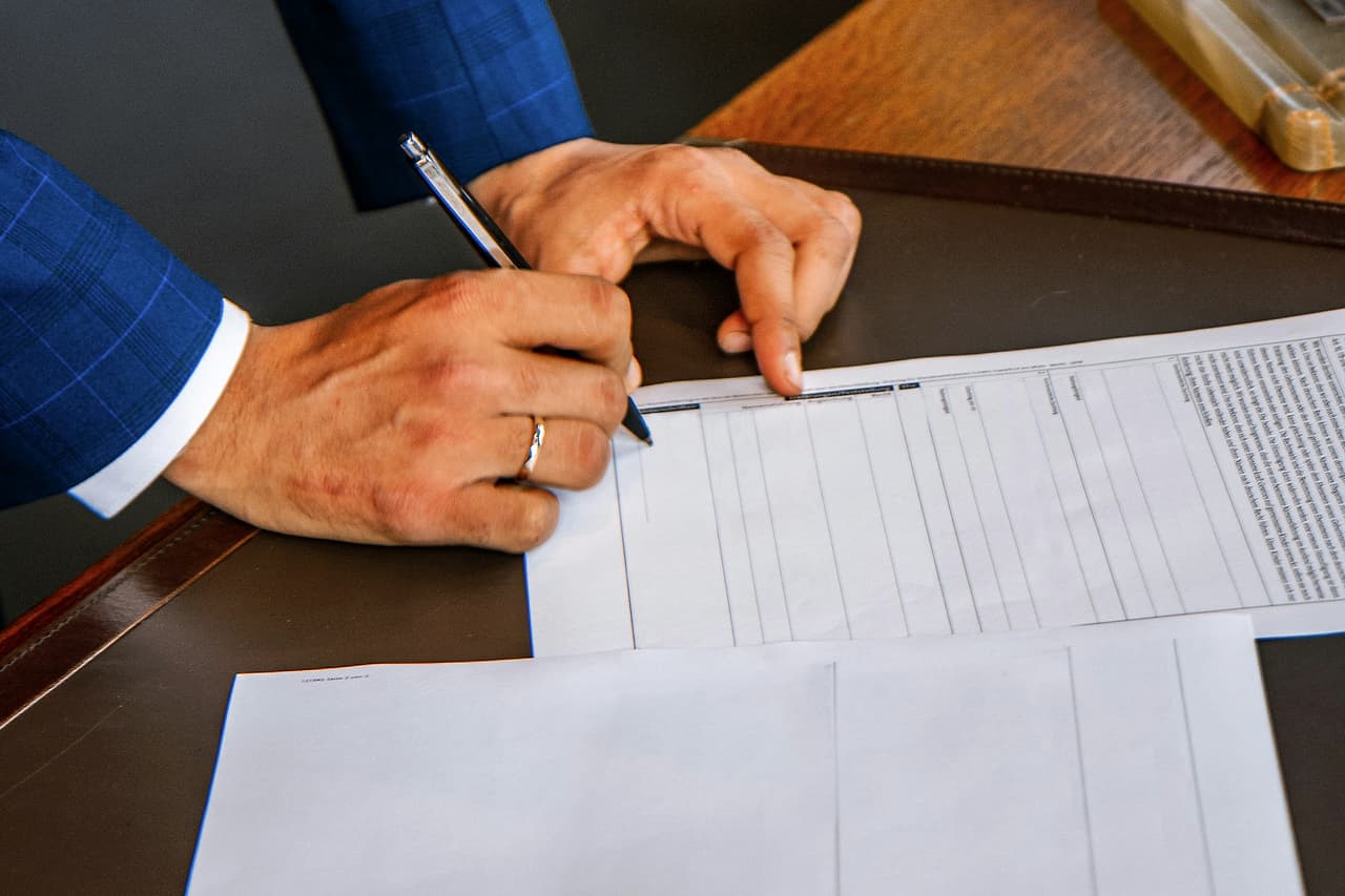 A hand with a pen filling in a printed form on a desk