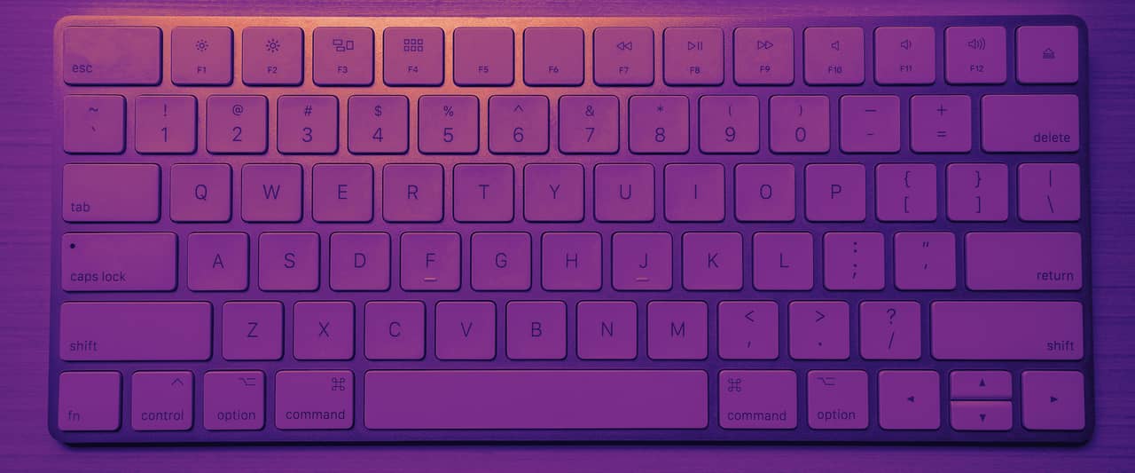 A white wireless computer keyboard on a light wooden desk