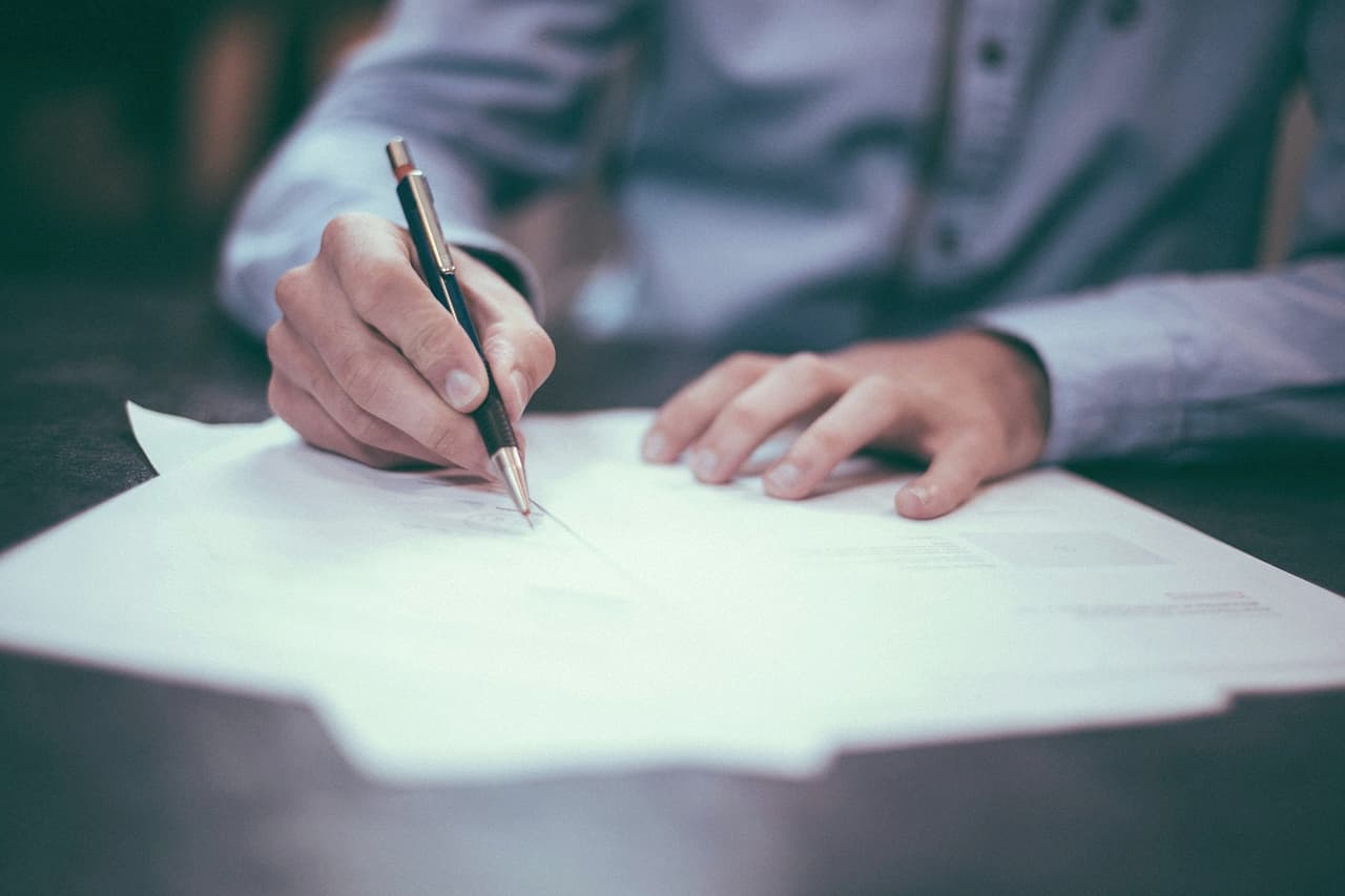 A person writing with a pen on a sheet of paper at a desk