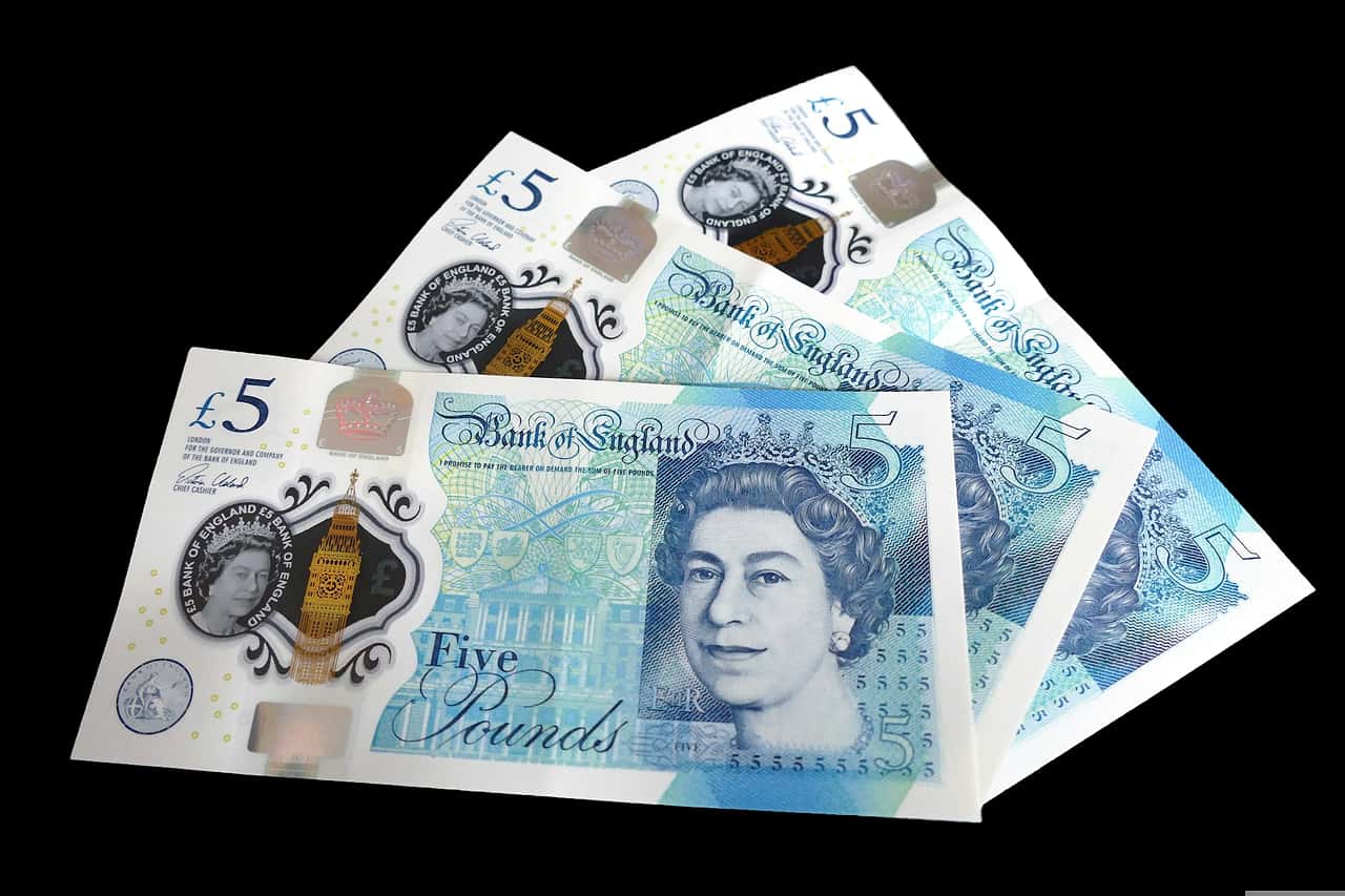 Three British five pound notes fanned out on a black background