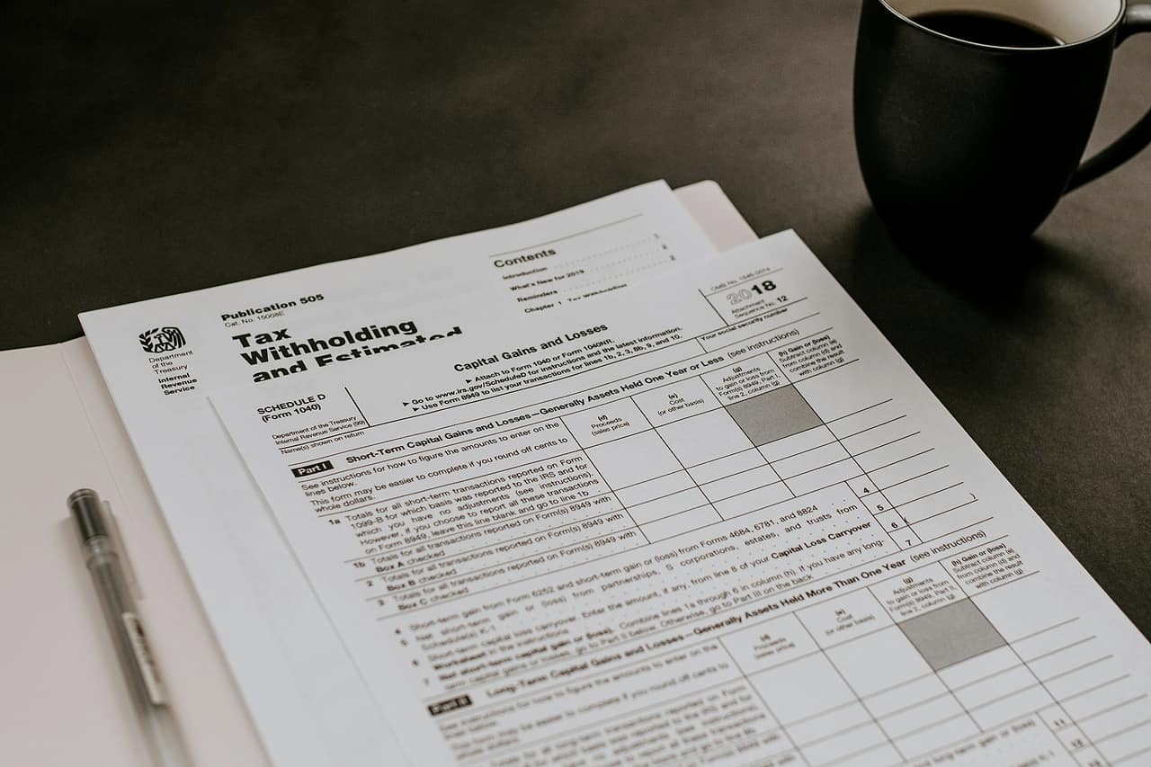 Printed financial forms and a pen beside a black mug on a dark table