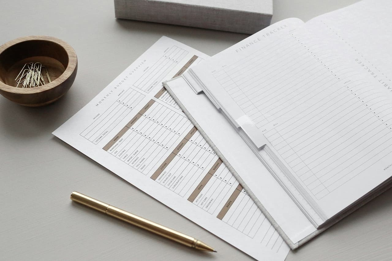 A budget planner with printed finance sheets, a gold pen and paper clips