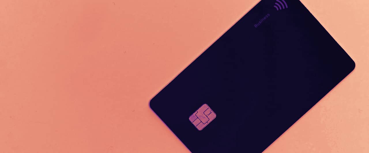 A plain black payment card with a chip lying on a white surface