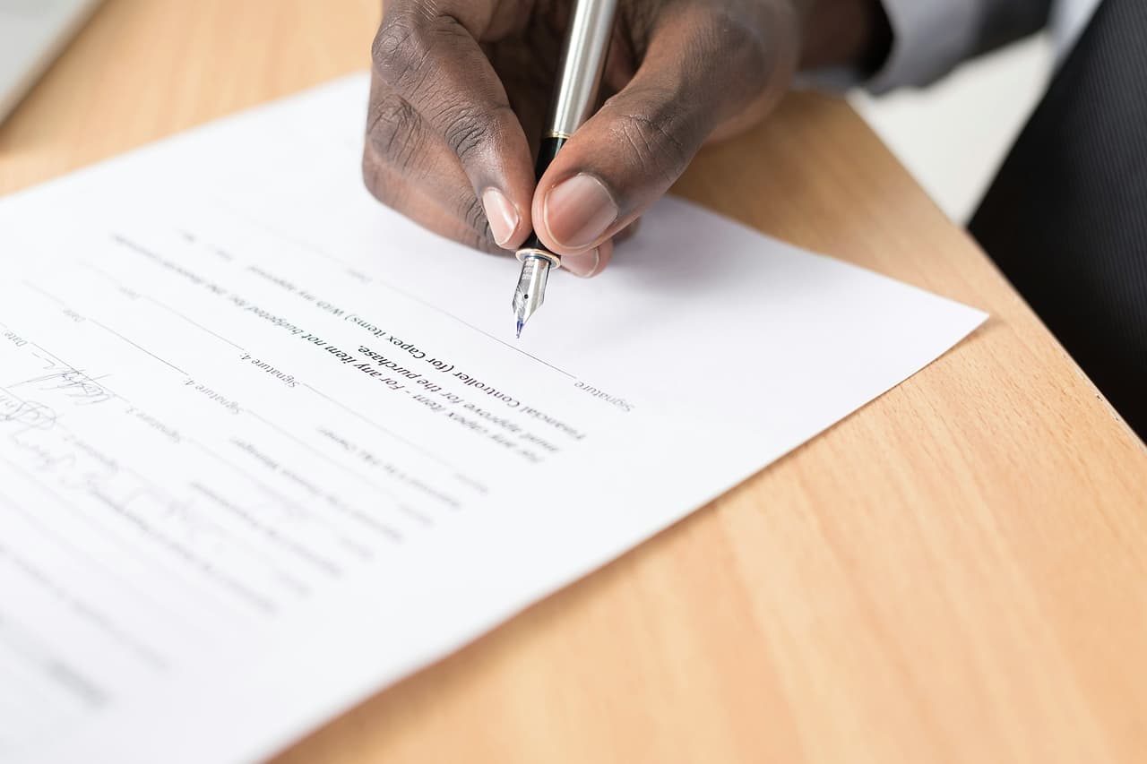 A hand with a fountain pen signing a printed document on a wooden desk