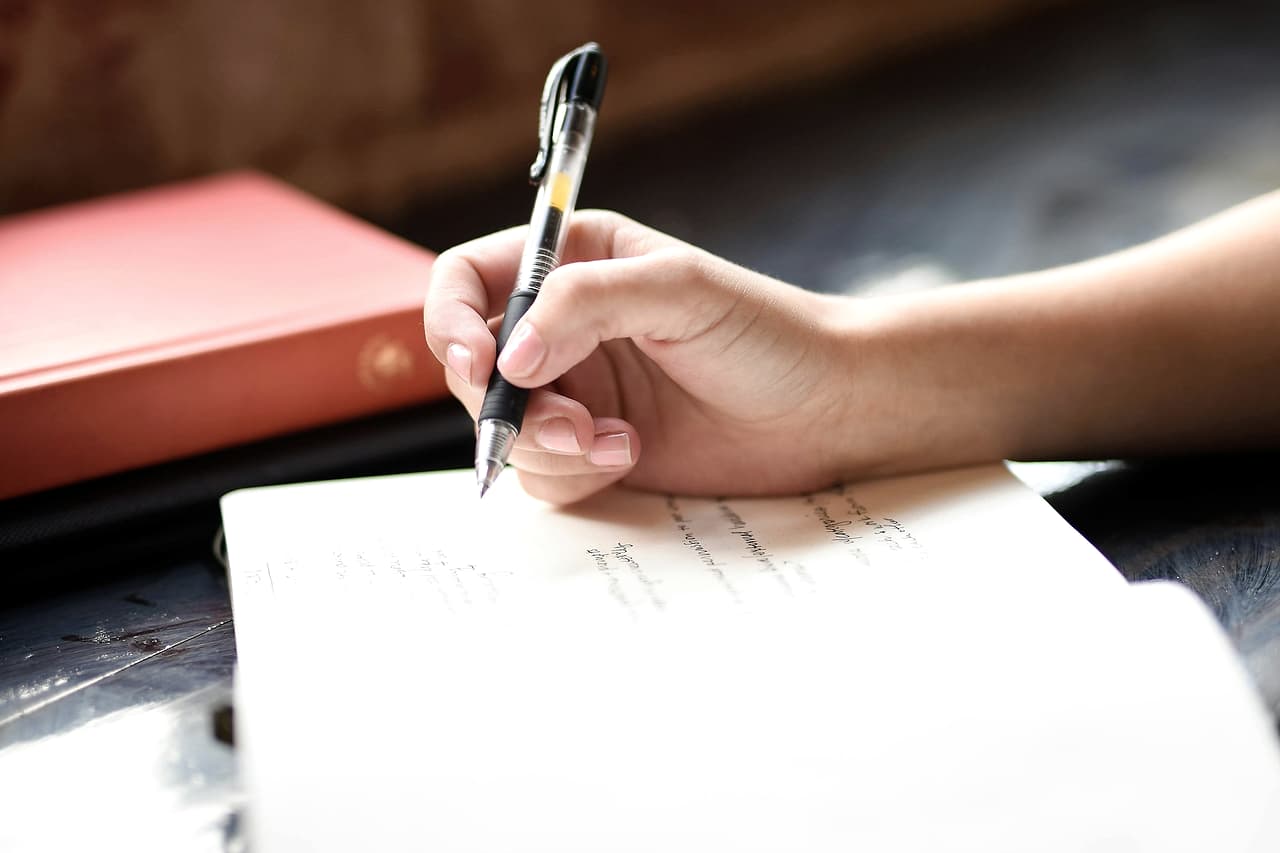 A hand writing notes on paper with a pen
