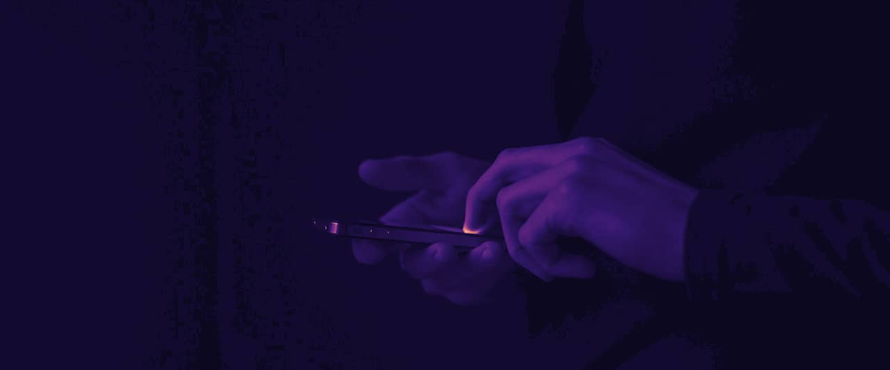 Two hands holding a lit smartphone against a dark background