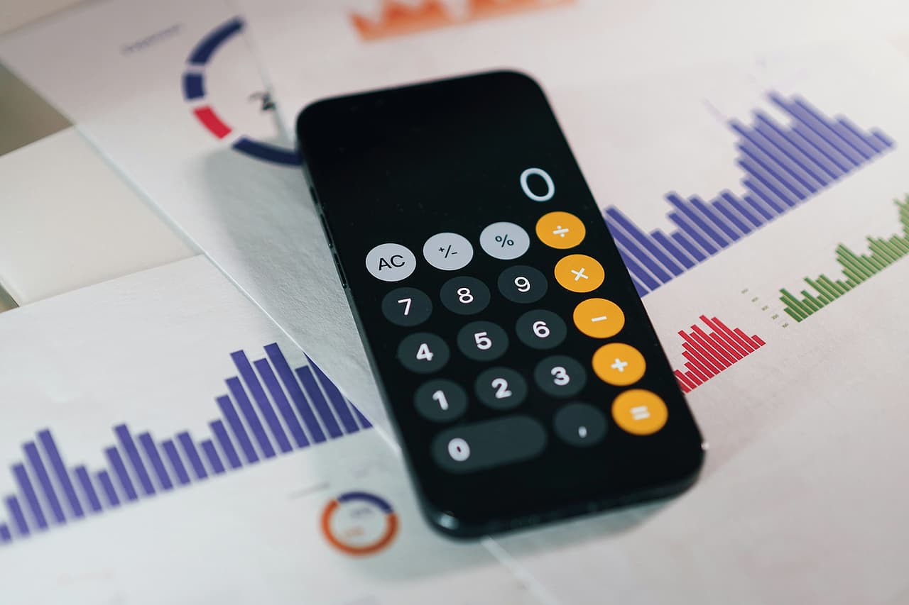 A phone showing a calculator app, lying on printed financial reports