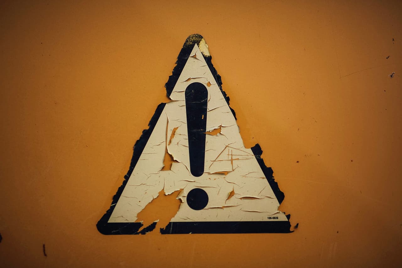 A worn triangular warning sign on an orange wall