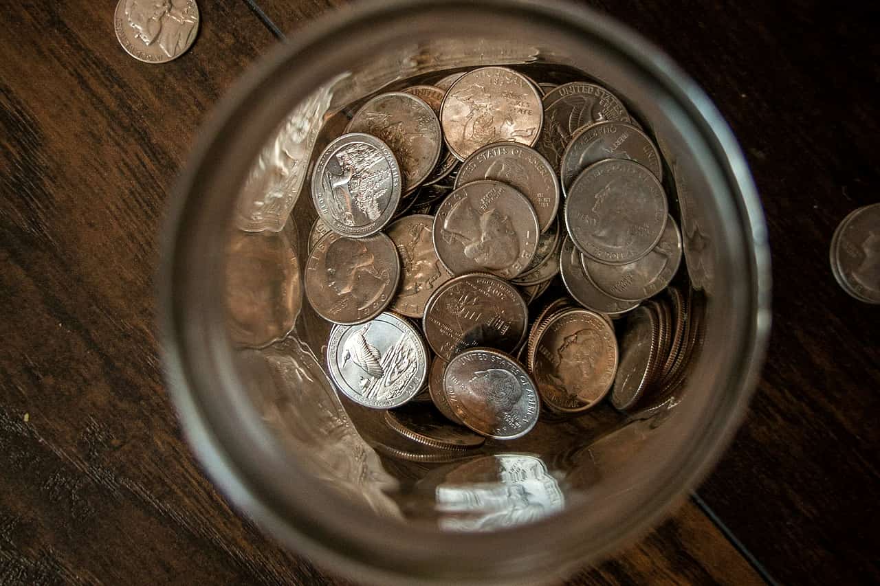 Coins seen from above inside a glass jar on a wooden table