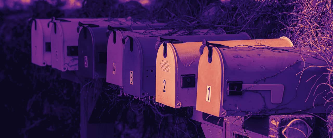 A row of painted mailboxes on posts in front of a hedge