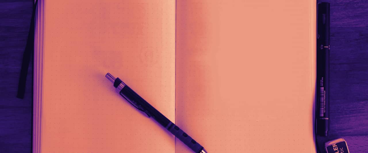 An open blank notebook with a pen lying across it on a wooden desk