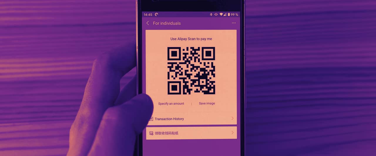 A hand holding a phone that displays a QR code above a wooden table