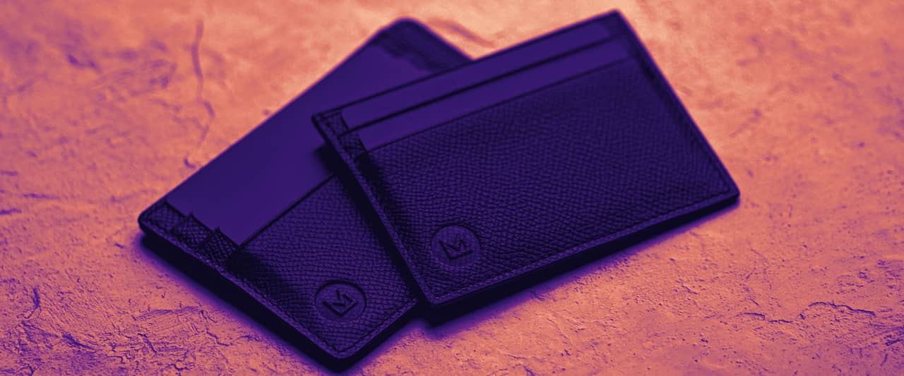 Two slim black card wallets on a pale textured surface