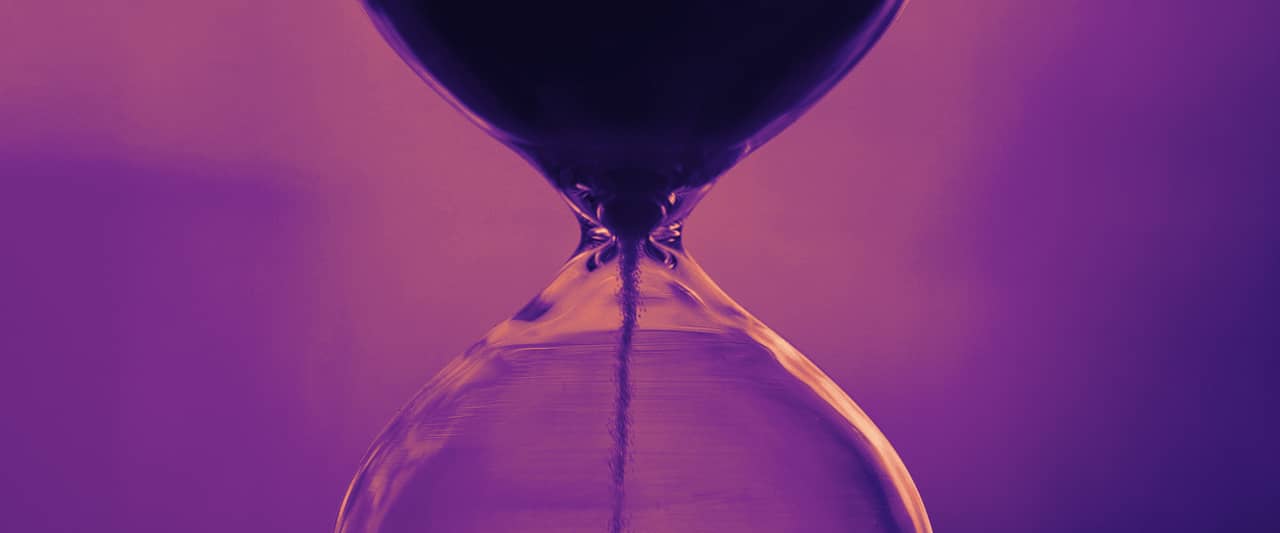 An hourglass with dark blue sand against a soft pink and violet background