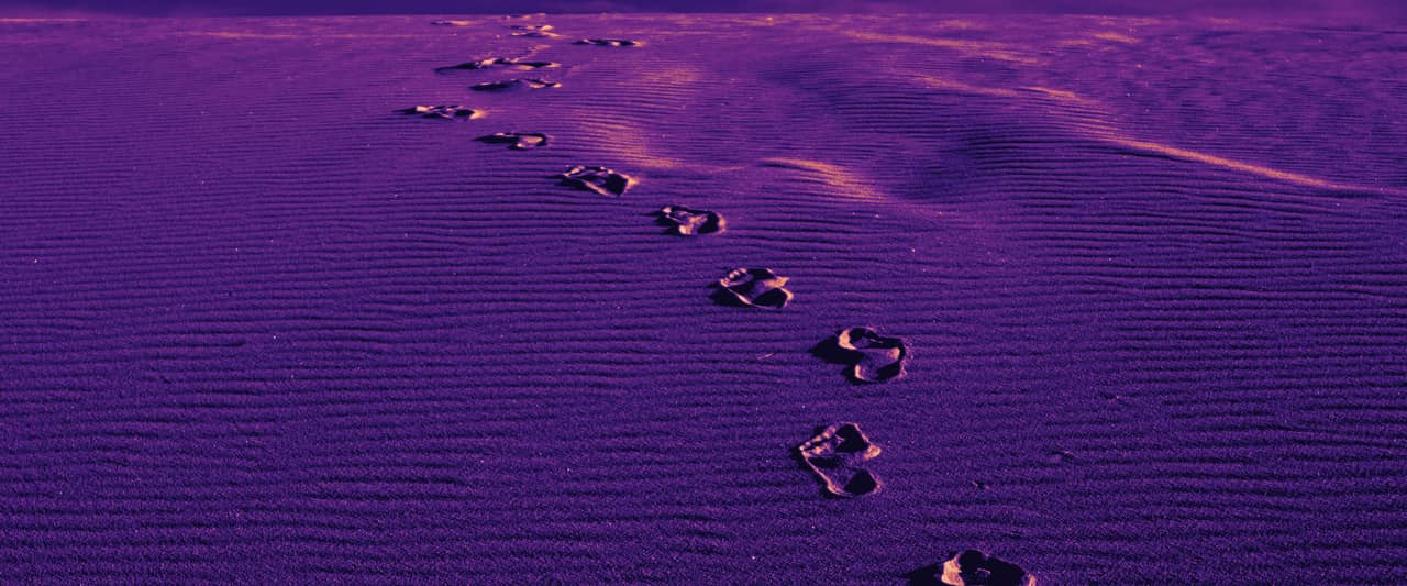 A line of footprints crossing white sand dunes under a blue sky
