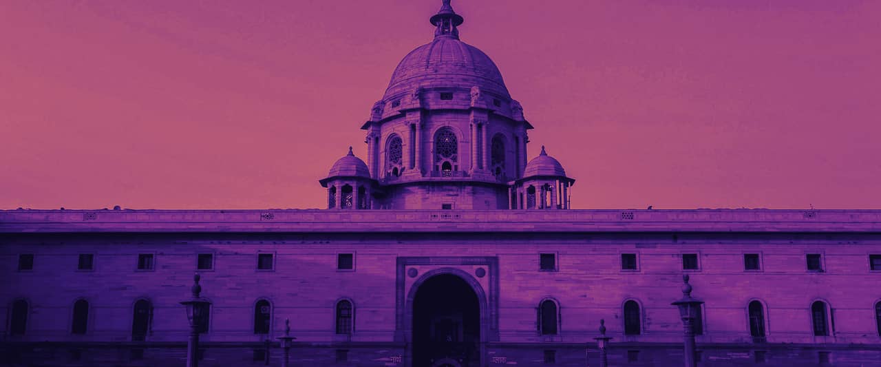 A sandstone government building with a central dome in Delhi under a blue sky