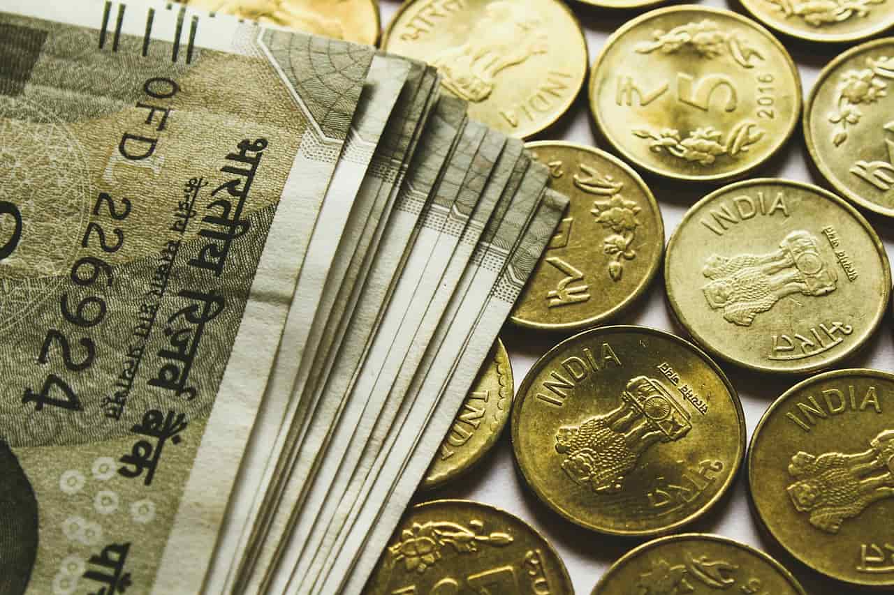 A bundle of Indian rupee notes beside rows of gold coloured rupee coins