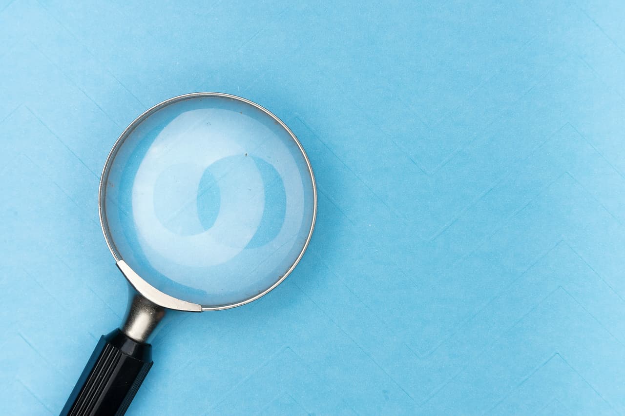 A magnifying glass lying on a plain light blue surface