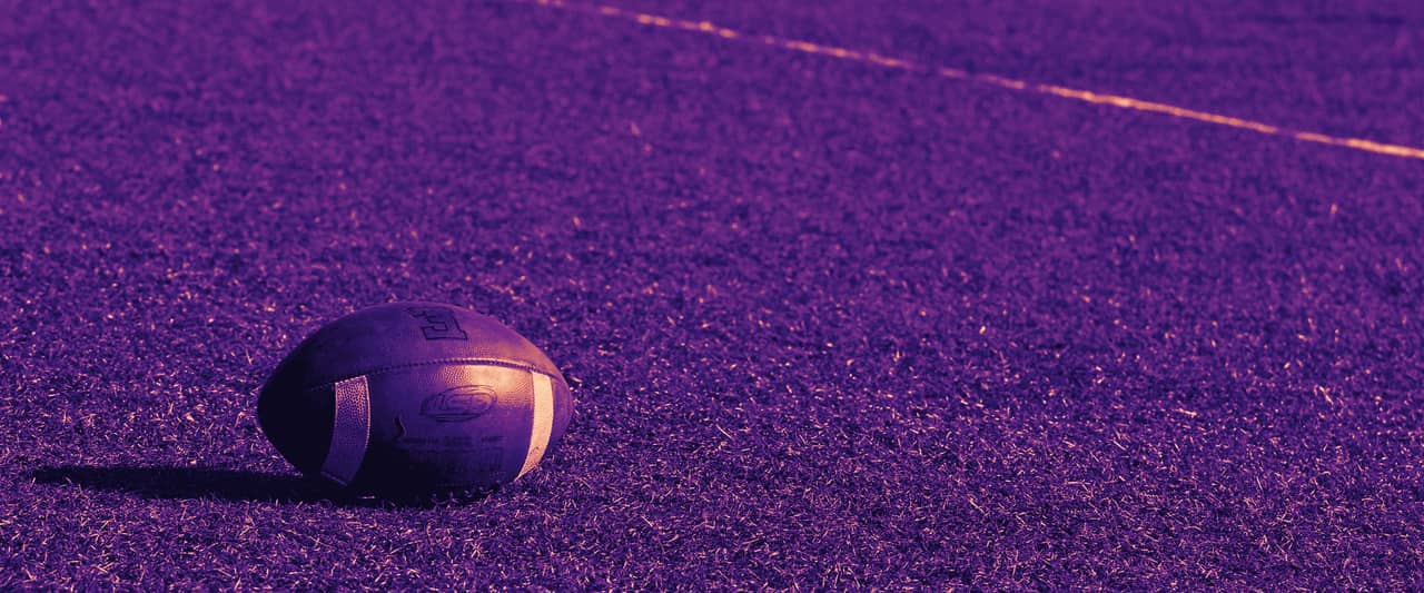 An American football resting on the grass of an empty field