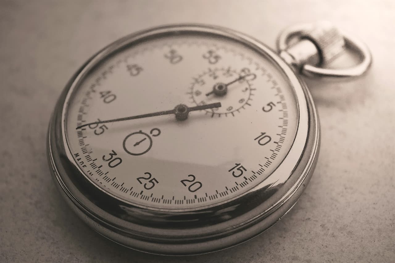 A silver stopwatch-style pocket watch on a grey surface