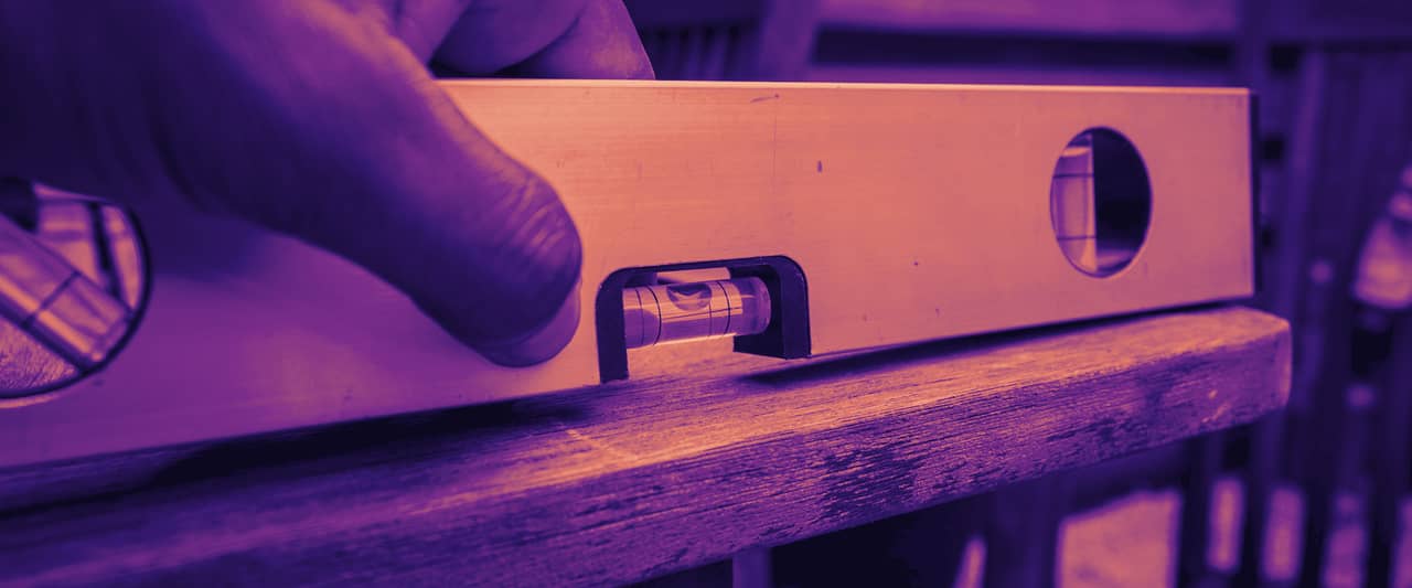 A hand resting a spirit level on a wooden table, the bubble centred