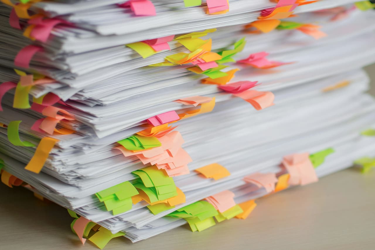 A tall stack of paper documents marked with coloured sticky tabs