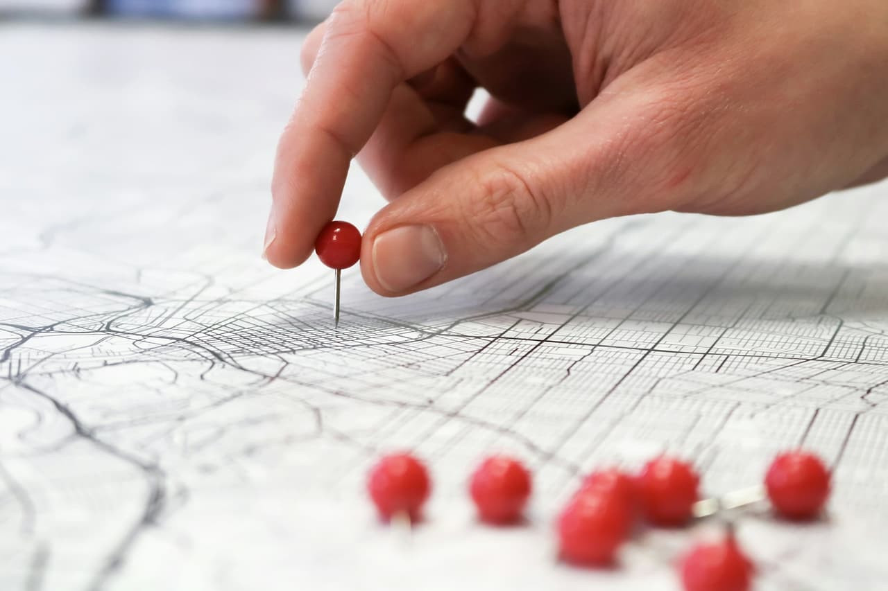 A hand placing red pins on a printed street map