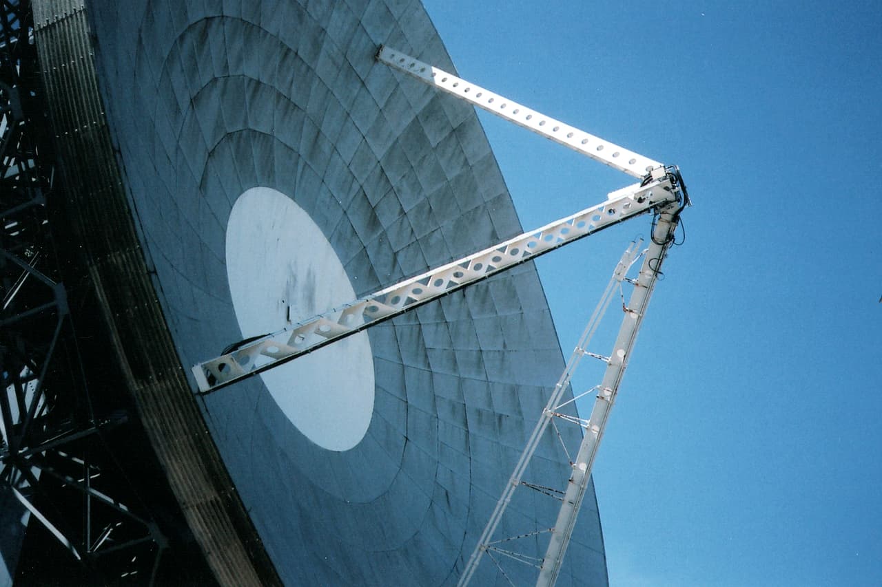 A white satellite dish angled against a blue sky