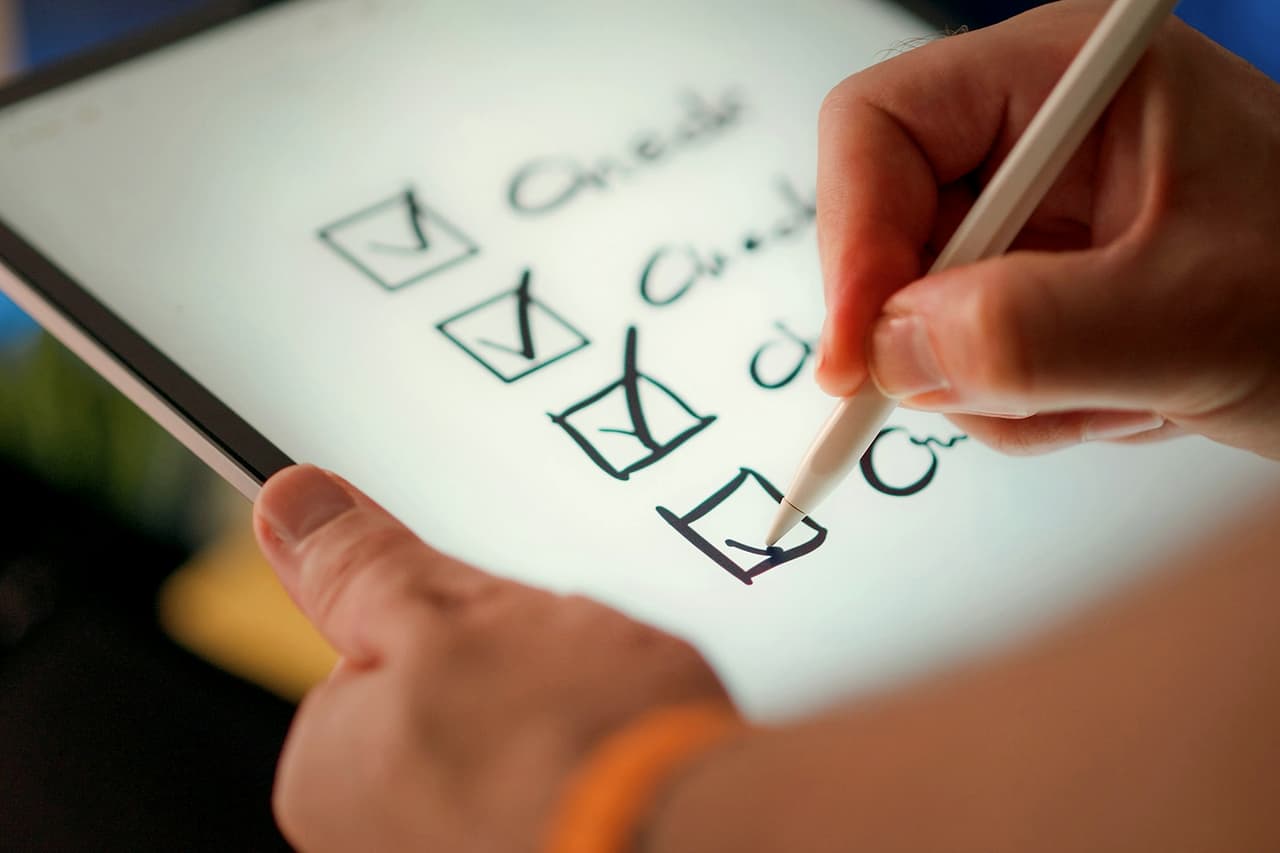 A hand ticking items on a checklist on a tablet with a stylus
