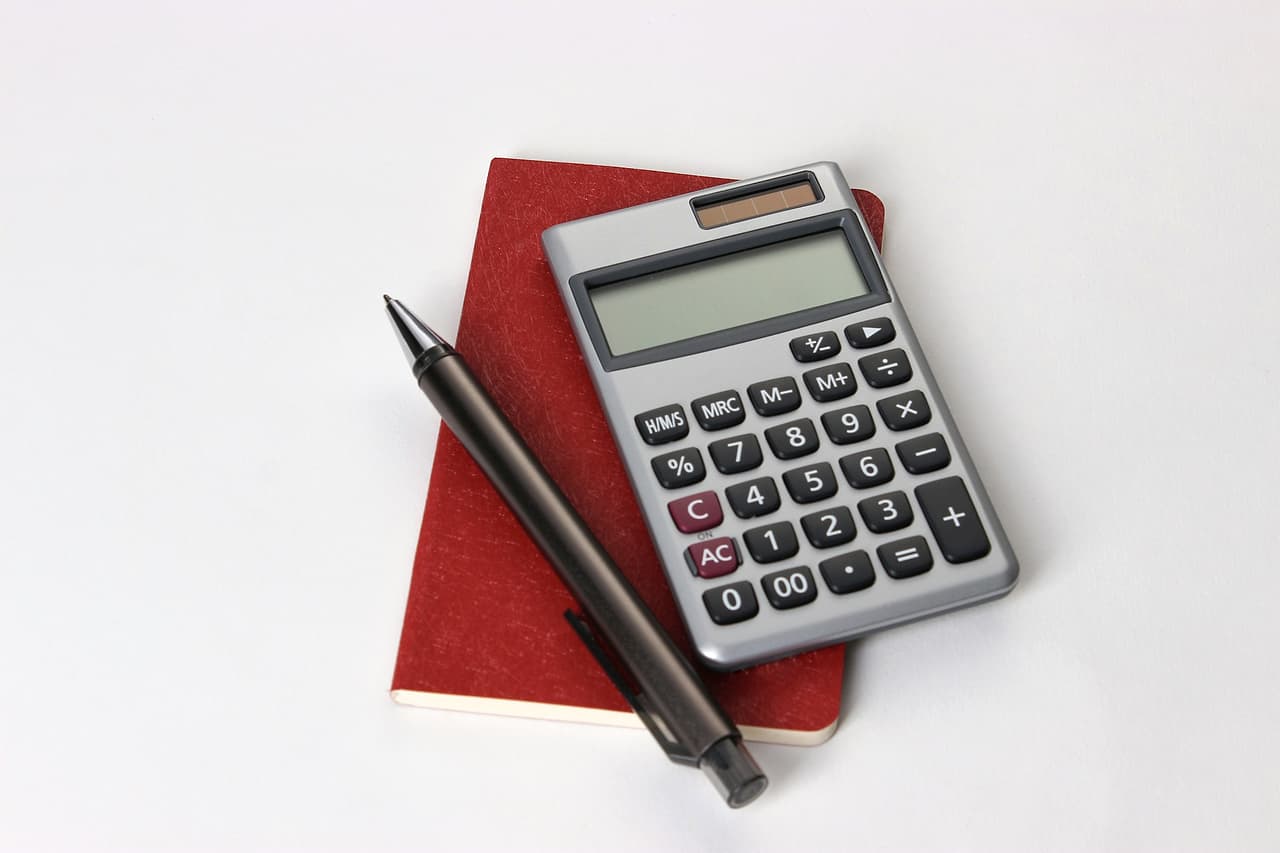 A silver calculator and a black pen beside books on a desk