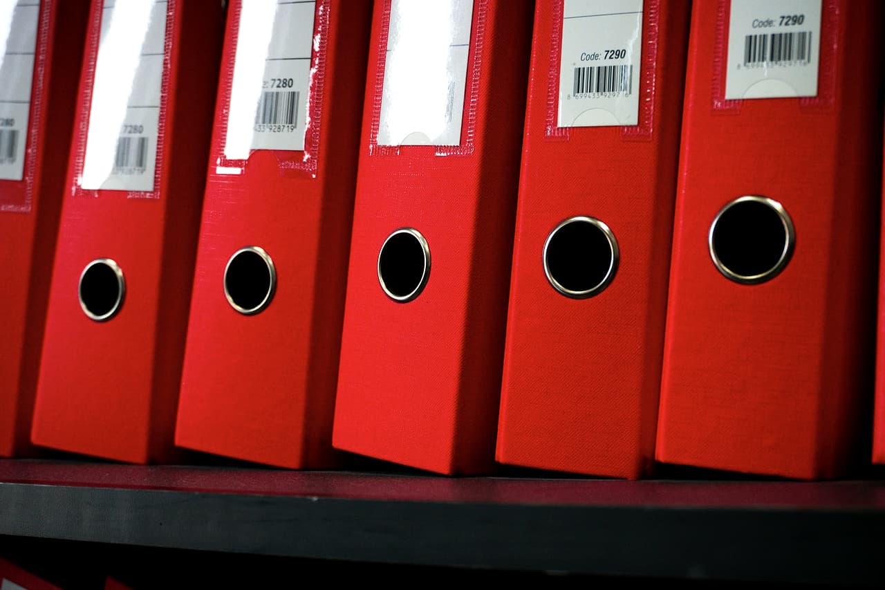 A row of red office folders with labels standing on a shelf