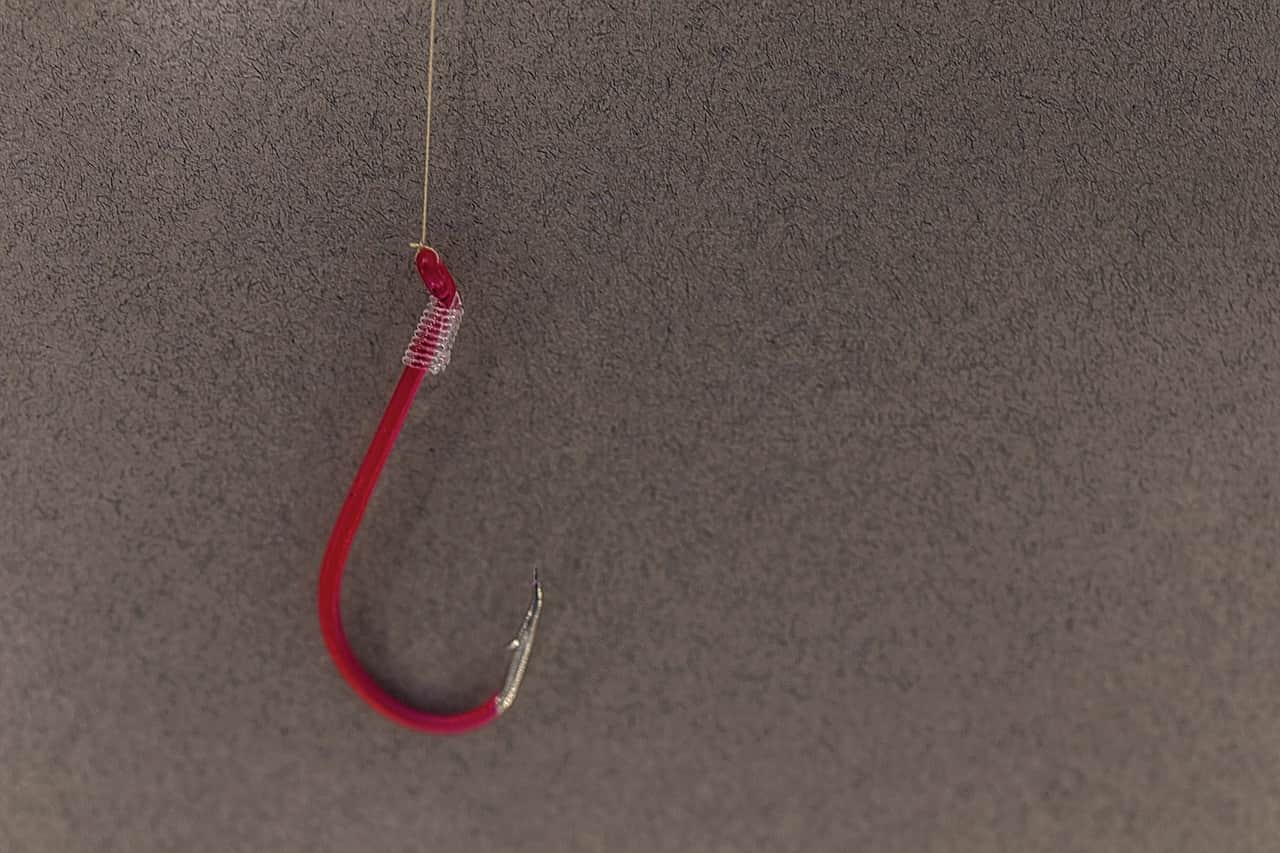 A red fishing hook hanging on a line against a grey background