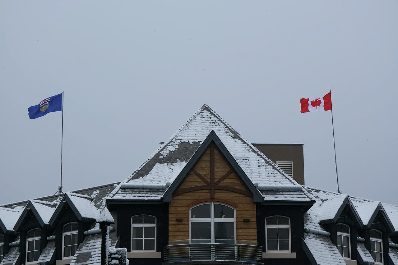 The Canadian and Alberta flags flying above a snowy roof in Banff