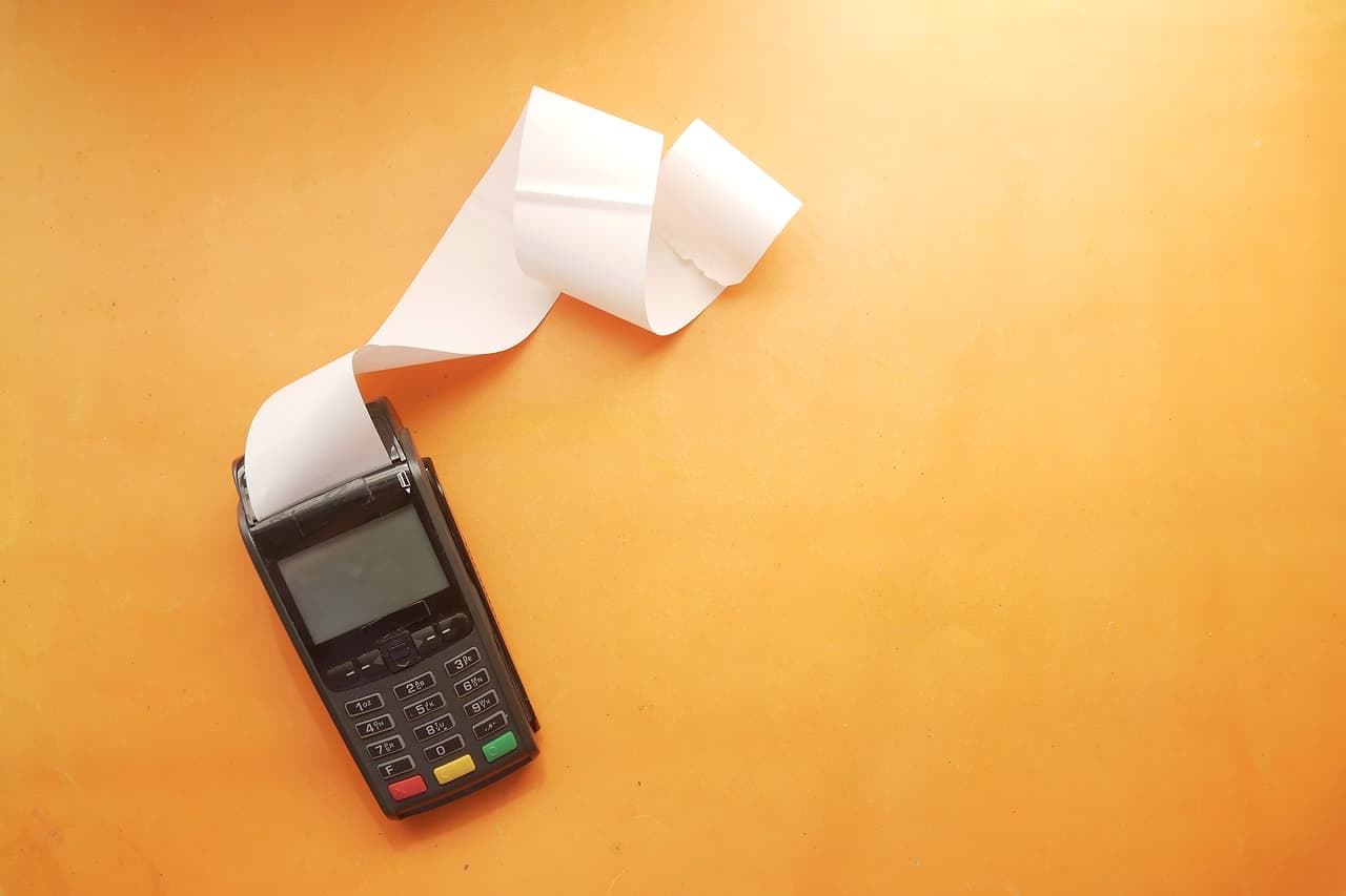 A card payment terminal printing a long paper receipt on an orange background