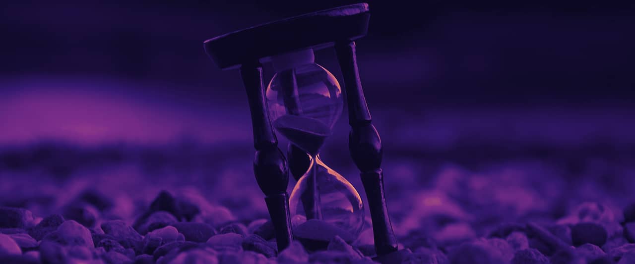 An hourglass with blue sand standing on pebbles
