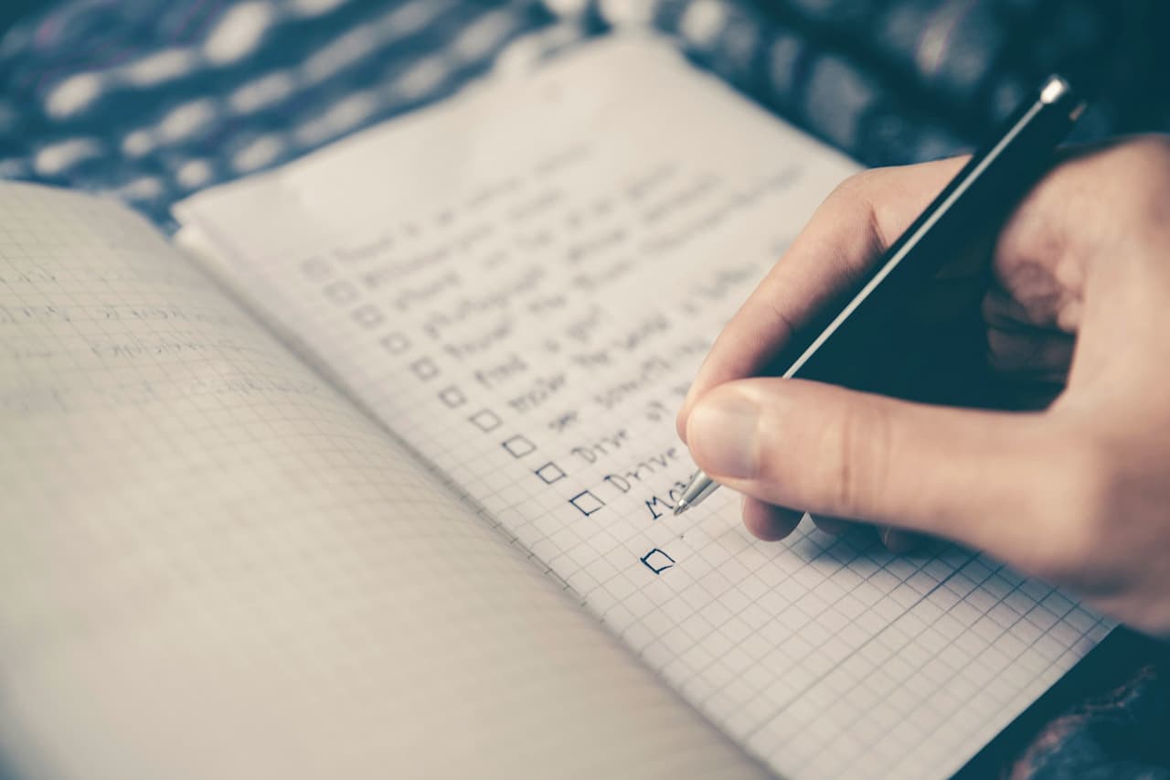 A hand writing in a lined notebook with a black pen