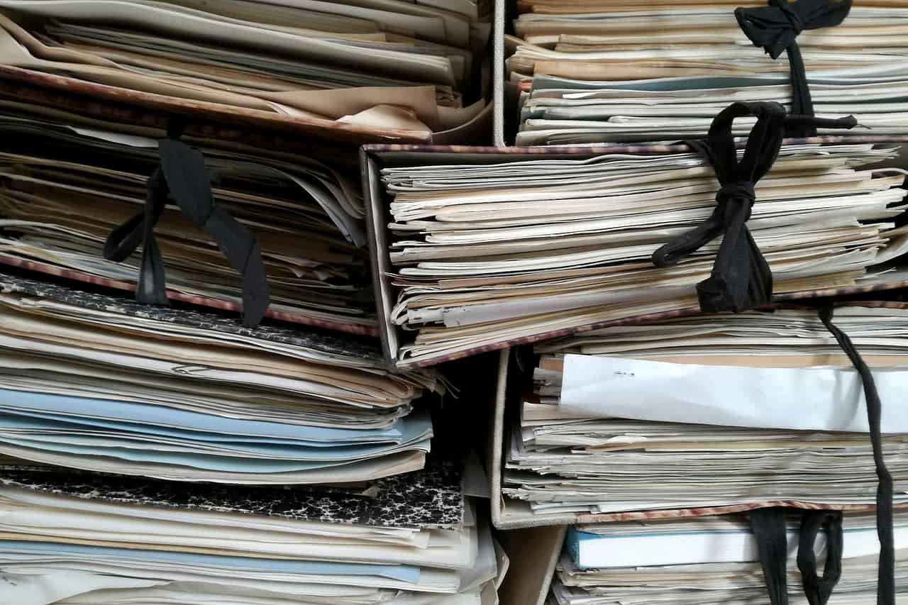 Bundles of old paper files tied together and stacked on a shelf