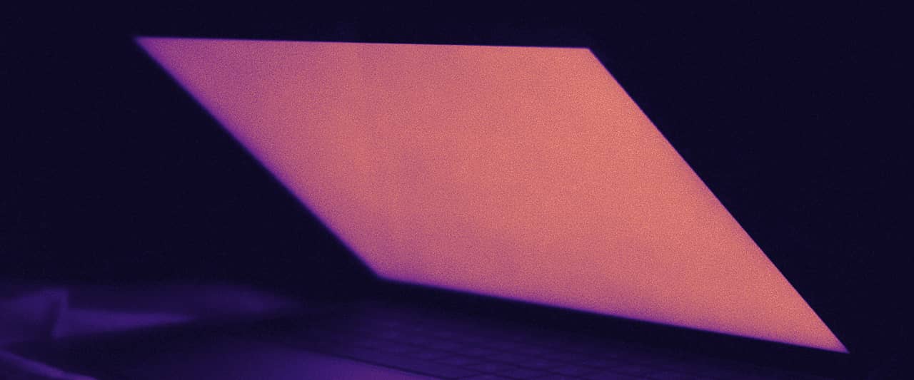 A half-open laptop glowing red in a dark room