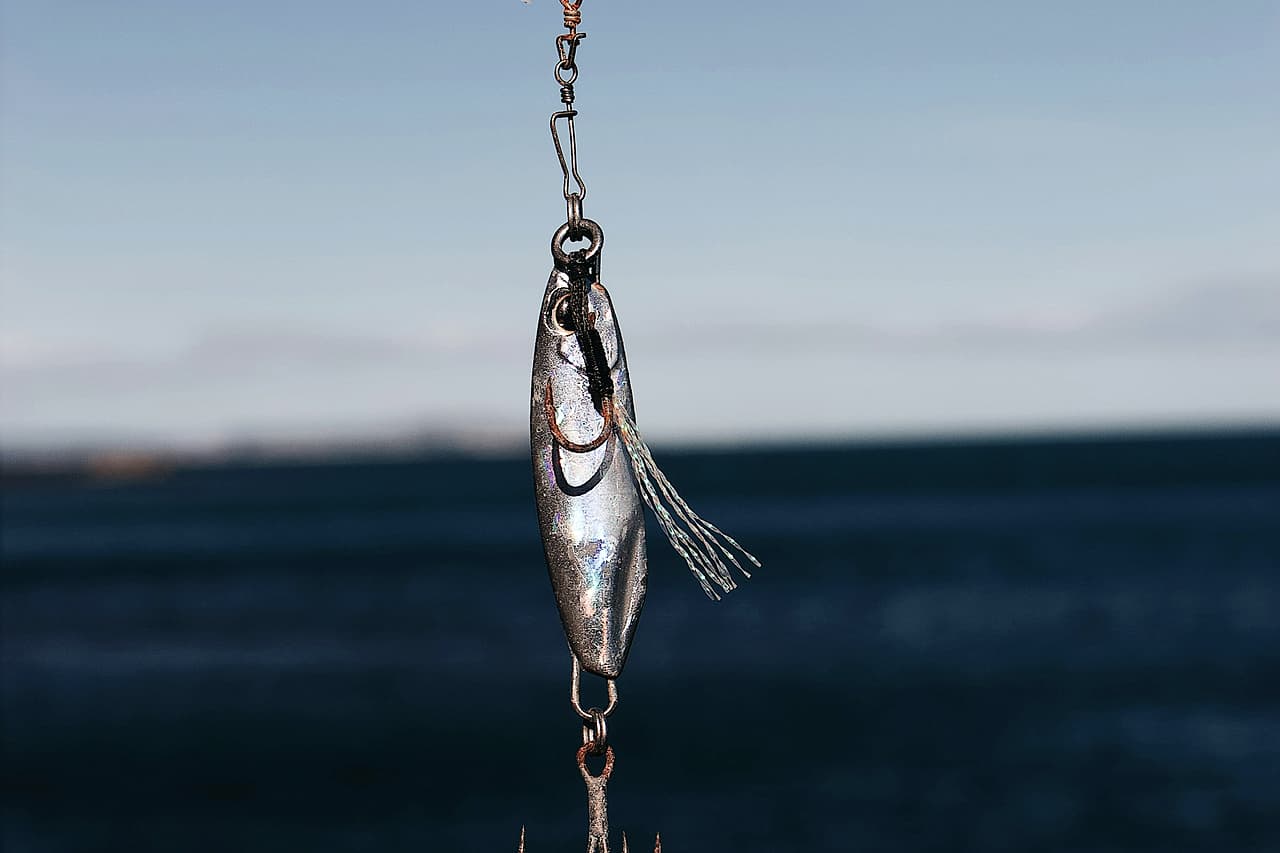 A grey fishing lure dangling on a line over dark water