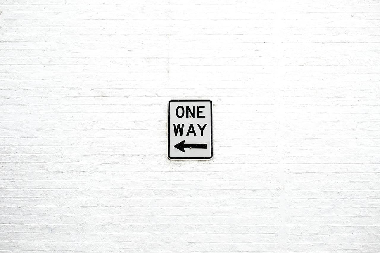 A One Way sign with a left arrow on a white wall